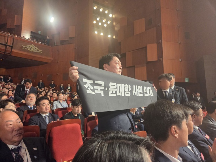 국민의힘 안철수 당대표 후보가 15일 광복절 경축식에 참석해 축사 중인 이재명 대통령을 향해 '조국·윤미향 사면 반대' 플래카드를 펼쳐 보이고 있다. (안철수 캠프 제공)