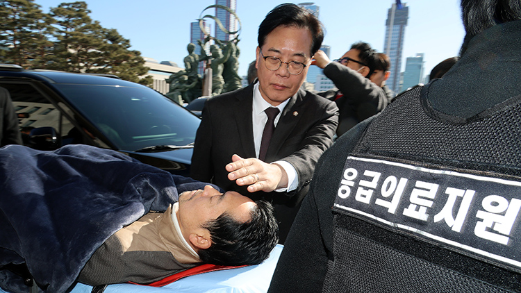 22일 통일교·공천헌금 '쌍특검' 수용을 요구하며 여드레째 단식을 이어가던 국민의힘 장동혁 대표가 건강 악화로 국회에서 병원으로 향하고 있다. 구급차에 탑승하는 장 대표 얼굴을 송언석 원내대표가 손으로 햇빛을 가려주고 있다. /연합뉴스